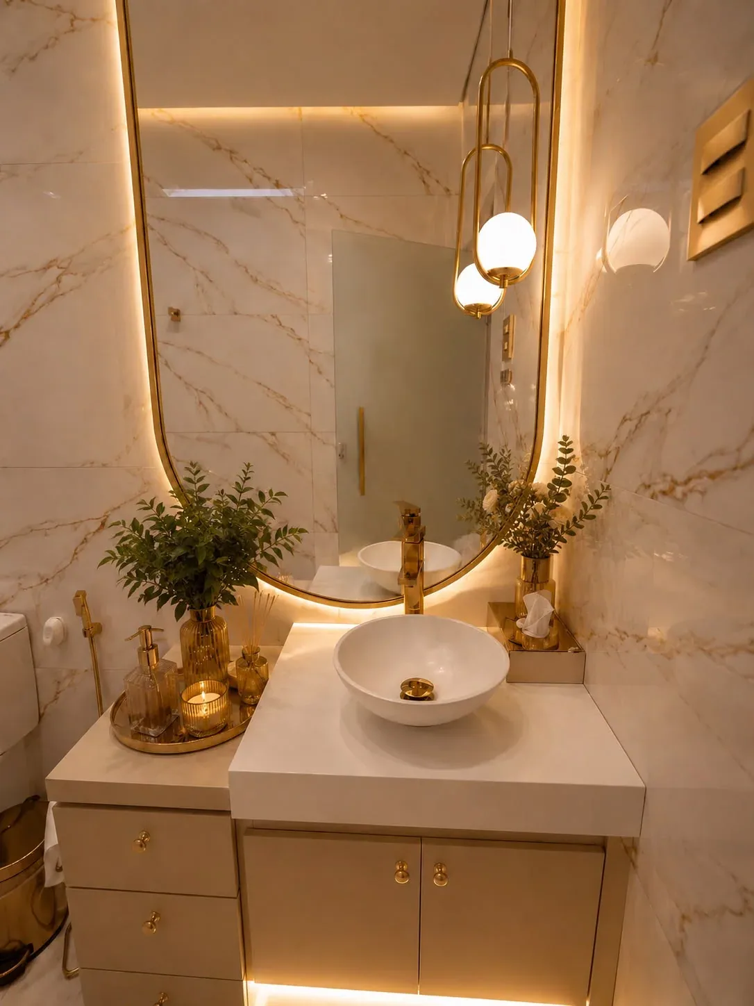Lavabo com cuba branca, espelho iluminado, revestimento marmorizado e metais dourados.
