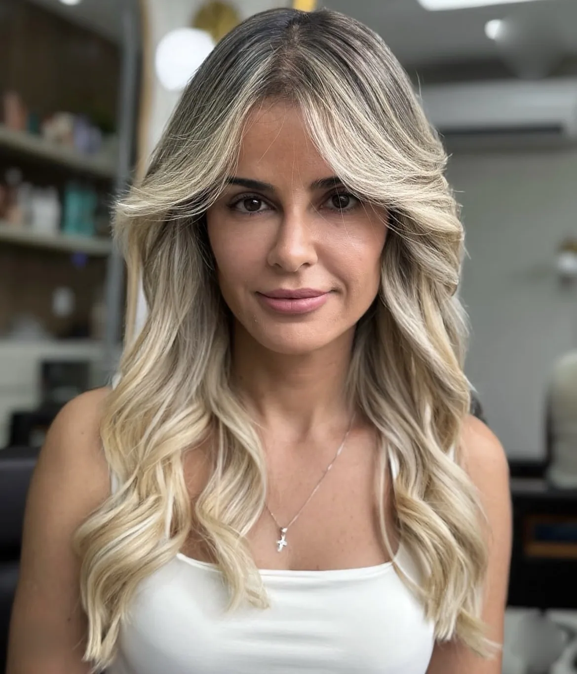 Cabelos loiros longos com mechas e ondas, emoldurando o rosto da cliente